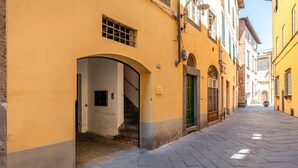 A narrow street with yellow buildings, an arched doorway, and a staircase leading to a second floor. - Toro's Home Lucca Apartment with Wi-Fi and Air Conditioning (Lucca)