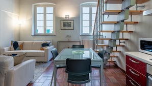 A modern living room with a glass dining table, a sofa, a staircase, and a kitchen area. - Toro's Home Lucca Apartment with Wi-Fi and Air Conditioning (Lucca)