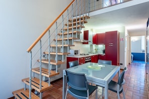 A modern kitchen with red cabinets, a wooden staircase, and a dining area with a glass table.