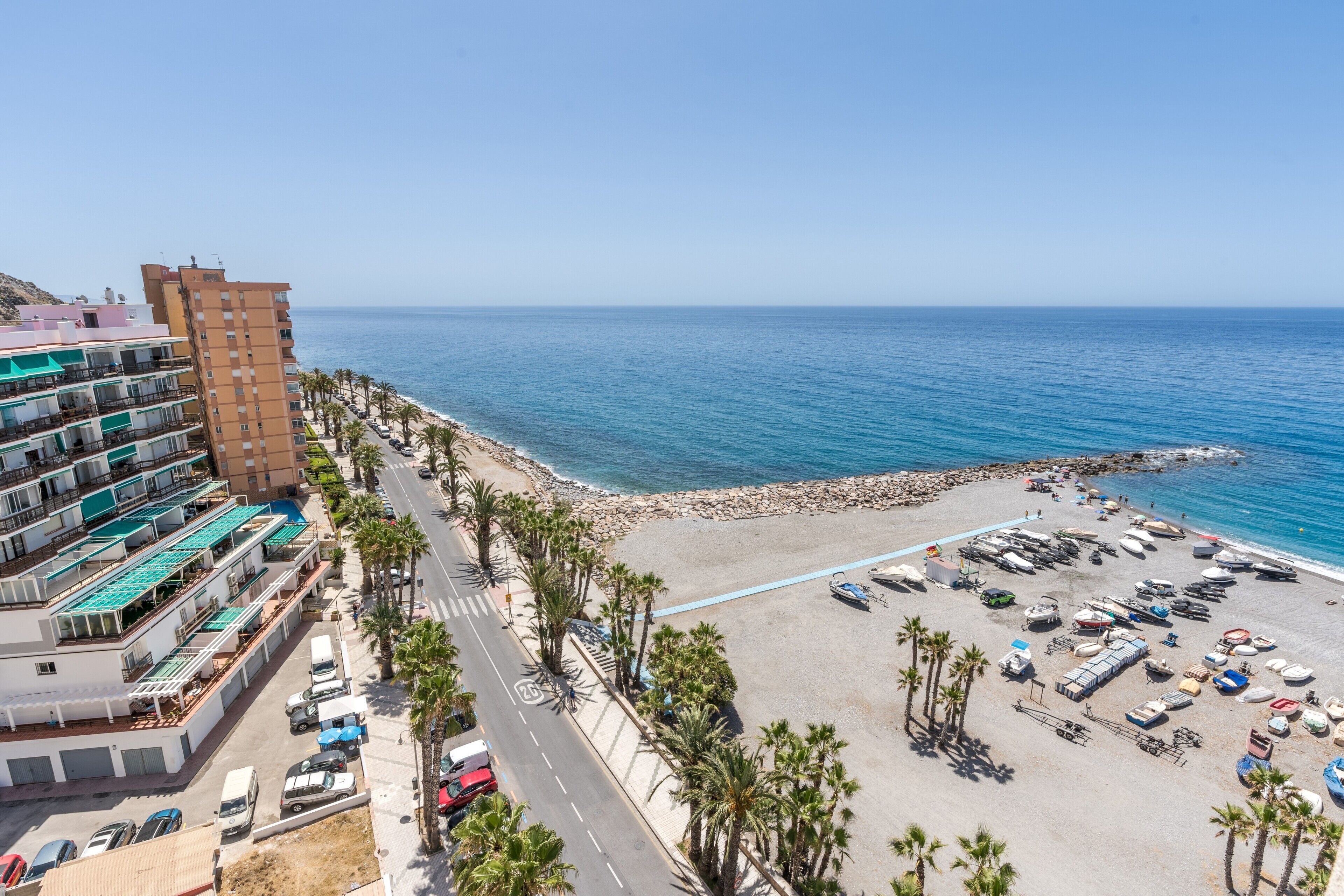 Un hôtel situé sur la côte, avec plusieurs étages, un parking et une zone de plage où sont amarrés des bateaux.