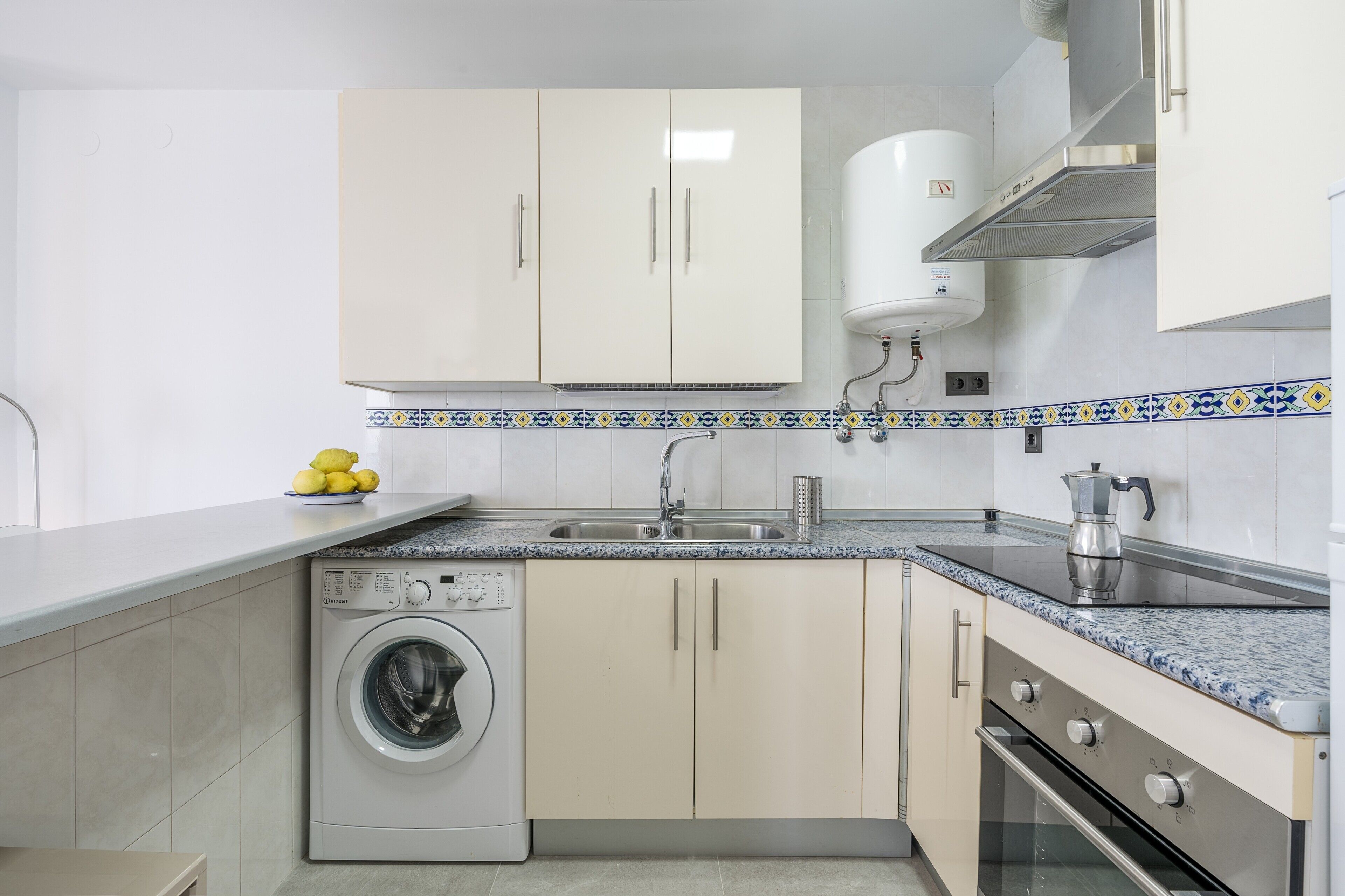 A kitchen with a washing machine, a sink, cabinets, and a stove.