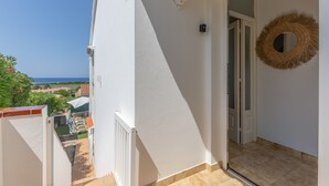 Un balcon donnant sur la mer, une porte blanche et une couronne en osier accrochée au mur.