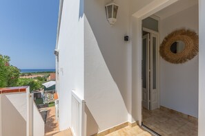 Een balkon met uitzicht op zee, een witte deur en een rieten krans aan de muur.