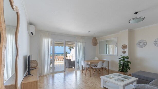 Un vaste espace de vie comprenant une table à manger, un canapé, un téléviseur posé sur un meuble en bois et un balcon avec vue.