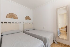 A bedroom with two beds, a large mirror, and two wall fans.
