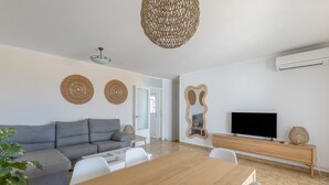 Un salon moderne avec un canapé gris, une table à manger en bois, un téléviseur et un luminaire en fibres tressées.