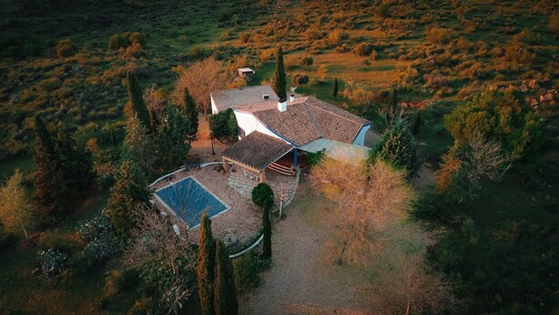 Vista aérea de una casa con piscina, rodeada de árboles y un paisaje montañoso.