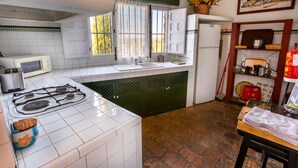 Una cocina con azulejos blancos, estufa a gas, pileta y refrigerador.