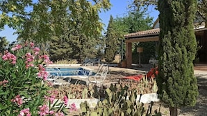 Una piscina con sillas de descanso, una pérgola, cactus y plantas con flores.