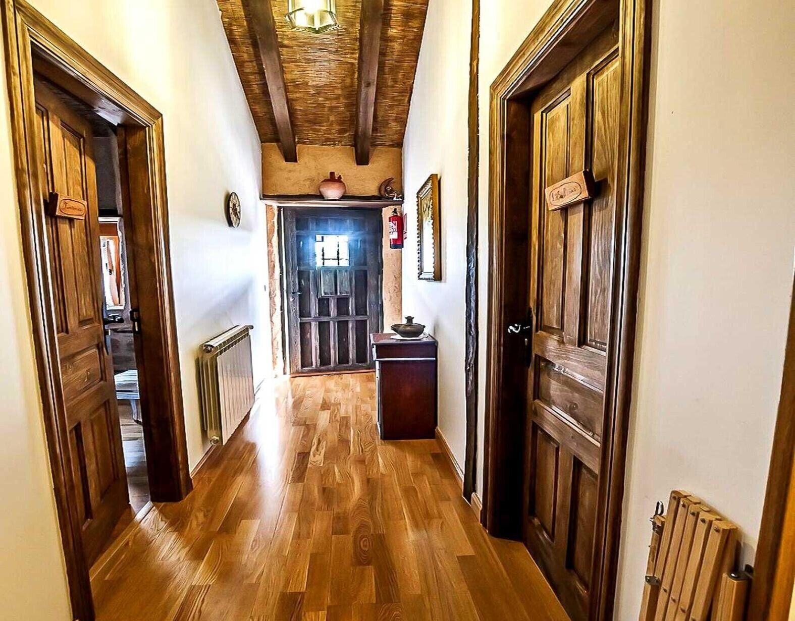 A hallway with wooden floors and doors, leading to a room with a radiator and a small table.