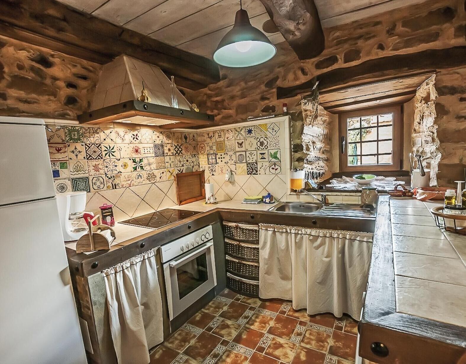 Eine rustikale Küche mit Steinwand, Fliesenrückwand, Holzboden und einem Fenster.