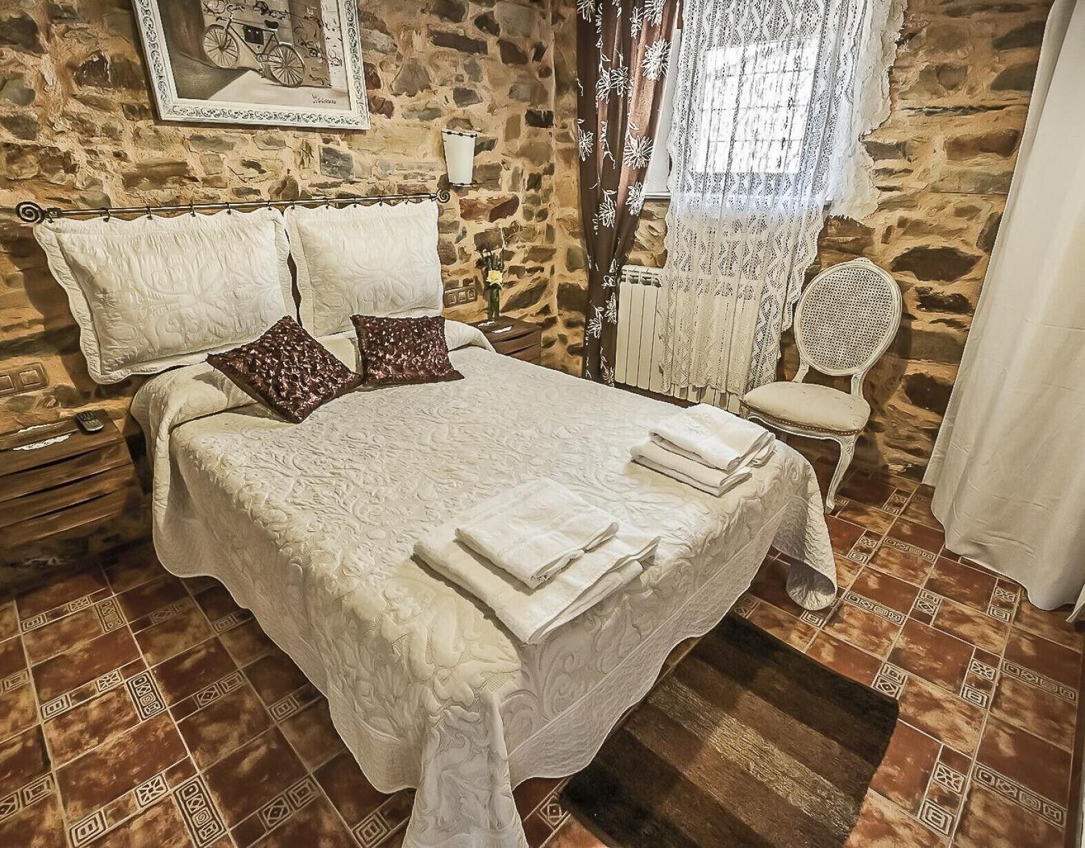 A bedroom with a stone wall, a bed with white linens, a chair, and a small table.