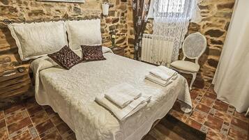 A bedroom with a stone wall, a bed with white linens, a chair, and a small table.