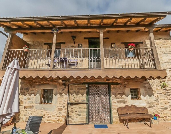 A two-story building with a balcony, stone walls, and a wooden pergola.