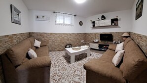 Een woonkamer met twee bruine banken, een witte salontafel, een televisie op een houten dressoir en een klok aan de muur.