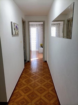 Un couloir avec un revêtement de sol à motifs, une porte donnant sur une autre pièce et un miroir accroché au mur.