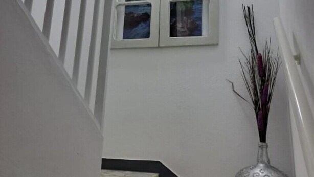 Een trap met een witte leuning, een raam met uitzicht op de stad, en een vaas met decoratieve takken.