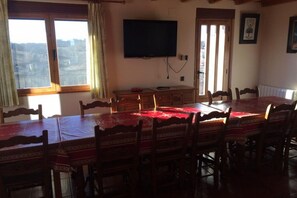 A dining room with a large table, chairs, a television, and a window with curtains.