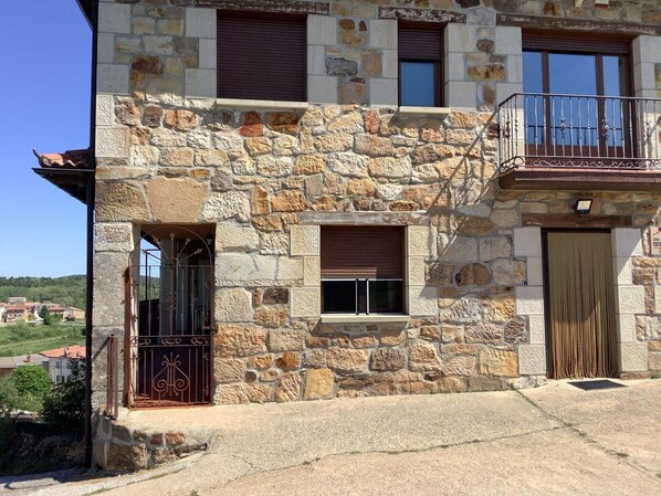 A stone building with a balcony, a gated entrance, and a small window.