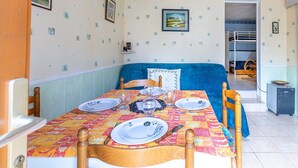 Een eetgedeelte met een tafel voor vier personen, een blauwe bank en een keuken die zichtbaar is door een open deur.