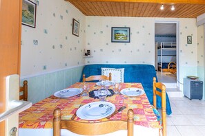 Un coin repas avec une table dressée pour quatre personnes, un canapé bleu et un espace cuisine visible à travers une porte ouverte.
