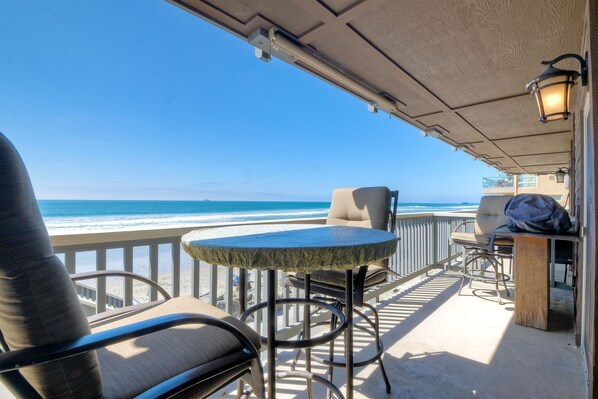 A balcony with a view of the ocean, a round table, and two chairs.
