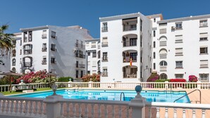 A hotel with a swimming pool, white exterior, balconies, and flower beds. - Apartment 'Manilva Home' with Mountain View, Wi-Fi and Air Conditioning (San Luis de Sabinillas)