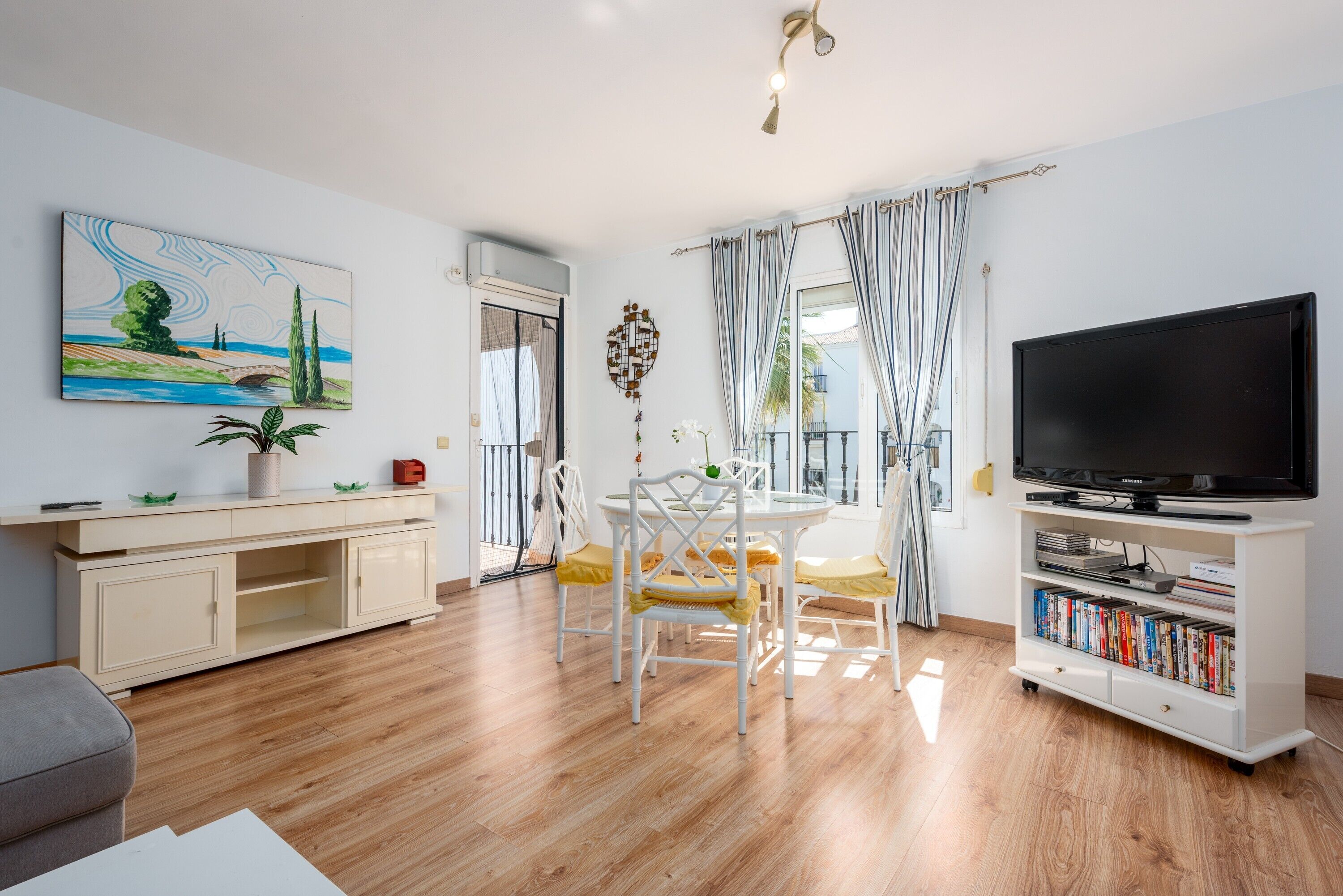 A living room with a TV, bookshelf, dining table, chairs, and artwork.