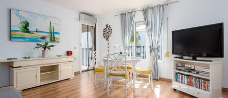 A living room with a TV, bookshelf, dining table, chairs, and artwork.