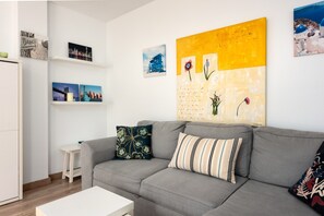 A living room with a grey sofa, a small white table, and wall art including a cityscape and a yellow abstract painting.