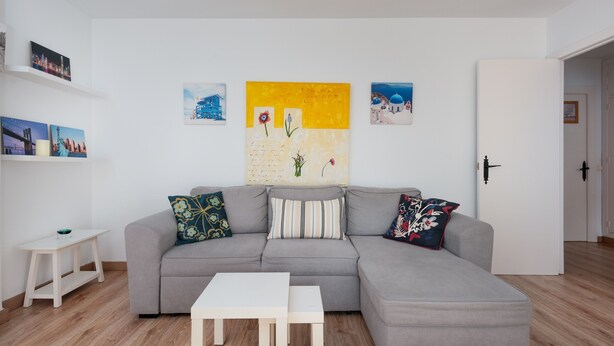 A modern living room with a grey sectional sofa, a white coffee table, and a small white side table. There are three framed artworks on the wall above the sofa. - Apartment 'Manilva Home' with Mountain View, Wi-Fi and Air Conditioning (San Luis de Sabinillas)