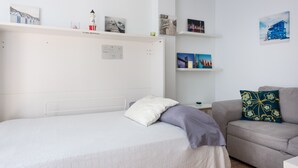A bedroom with a bed, a nightstand, a sofa, and wall-mounted shelves with various items. - Apartment 'Manilva Home' with Mountain View, Wi-Fi and Air Conditioning (San Luis de Sabinillas)