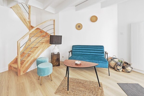 A modern living room with a wooden staircase, a blue sofa, a round coffee table, and woven baskets.