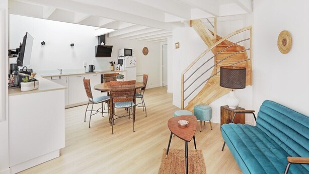 Una cucina moderna con mobili bianchi, un'area pranzo con sedie in vimini, un divano blu e una scala a chiocciola.