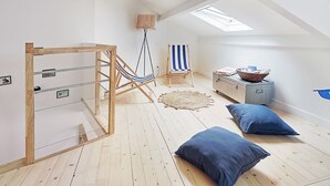 Una stanza con pavimento in legno, un'amaca, una sedia a righe, un tavolino con un cesto e una finestra a lucernario sul soffitto.