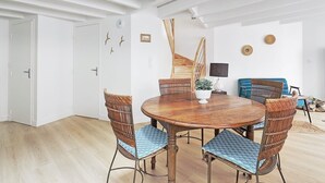 Una stanza con un tavolo da pranzo in legno, sedie in vimini, un divano blu e una scala.