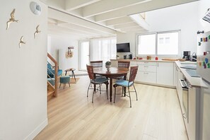 A modern kitchen with a dining area, wooden flooring, and a staircase leading to another room.