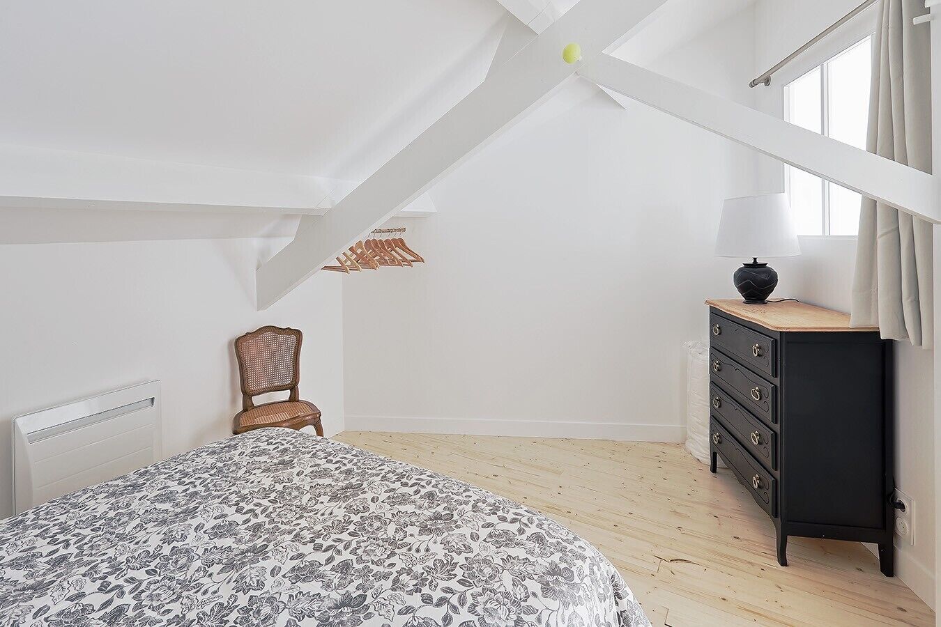 A bedroom with a bed, a chair, a dresser, and a window with curtains.