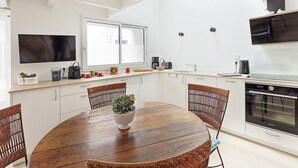 Una cucina moderna con mobili bianchi, un tavolo da pranzo in legno, sedie in vimini, una pianta in vaso e un'ampia finestra.