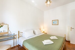 Quarto com cama, mesa de cabeceira, luminária e radiador.