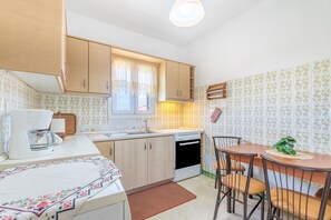 Uma cozinha compacta com armários de madeira, forno embutido, pia e um espaço de refeições com mesa e cadeiras.
