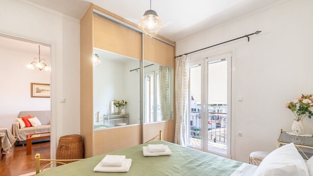 Une chambre avec un lit, une chaise, une petite table, un miroir et une vue sur le balcon.