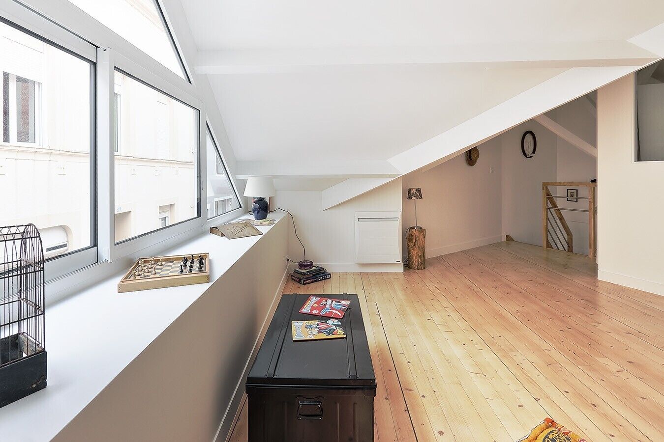 Ein geräumiges Dachzimmer mit geneigtem Dach, großen Fenstern und Holzboden.