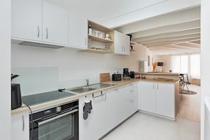 Une cuisine moderne avec des meubles blancs, un four encastré, une machine à café et un coin repas comprenant une table et des chaises.