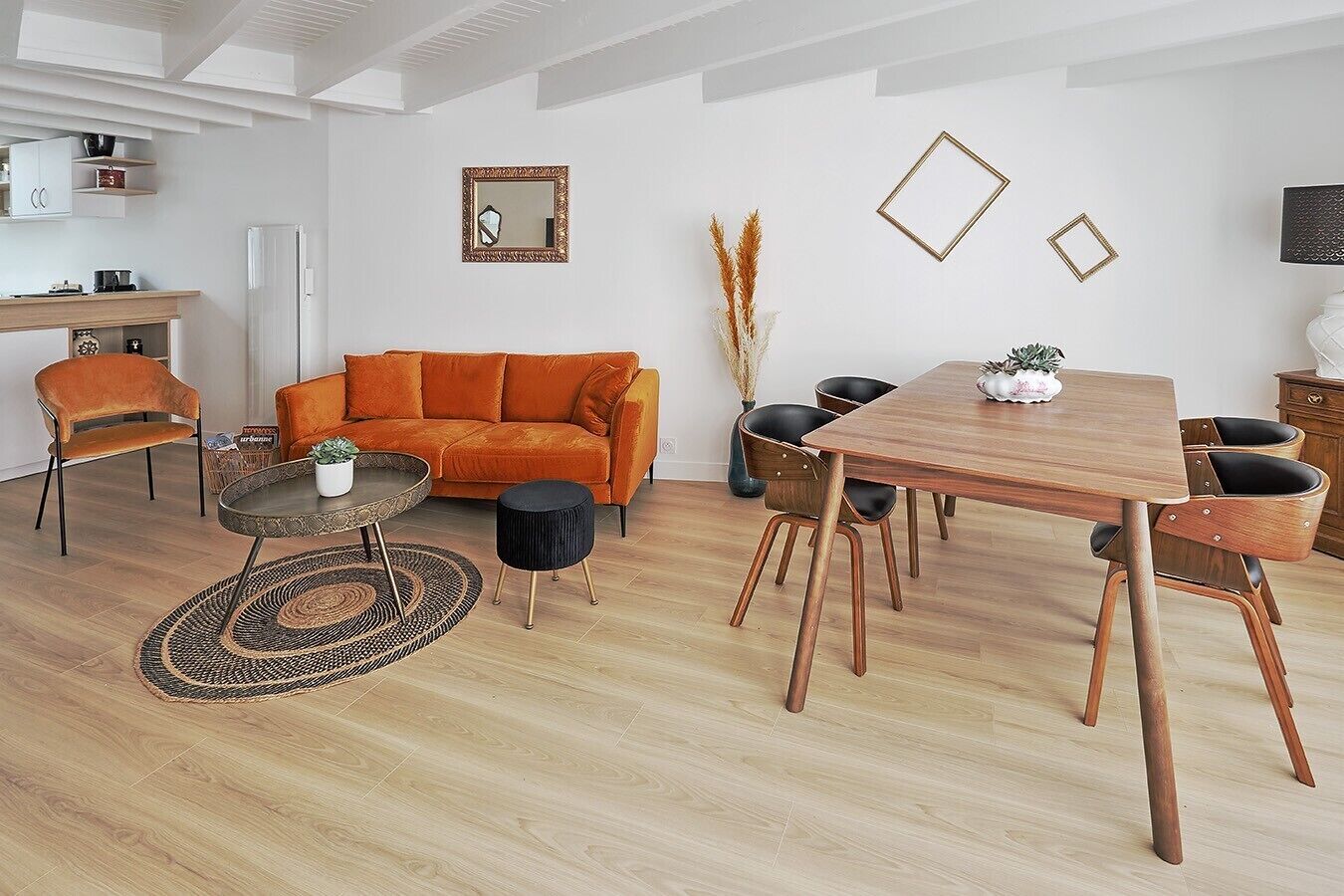A modern living room with a sofa, coffee table, chairs, a dining table, and a kitchen area.