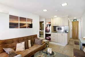 A modern living room with a brown sofa, a glass coffee table, and a kitchen area with a microwave and cabinets.