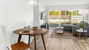 Una sala de estar moderna con una mesa redonda de madera, un sofá gris y un ventanal con vistas a la vegetación.