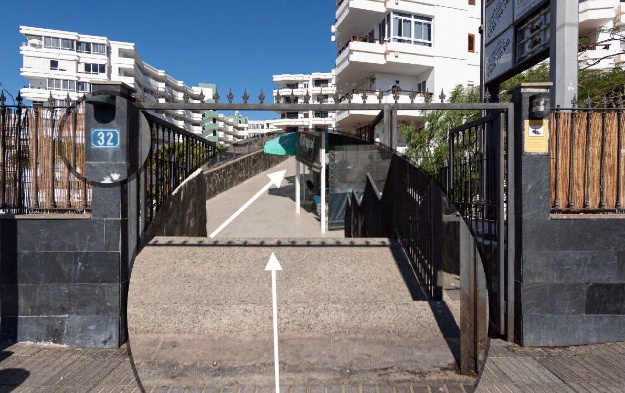 Une entrée fermée par un portail mène à un immeuble. Un chemin bien dégagé conduit à l’entrée, un panneau indique le numéro 32, et une flèche directionnelle est peinte sur le sol.