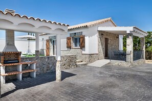 Un espace extérieur aménagé avec un barbecue, des murs en pierre et un coin salon abrité.