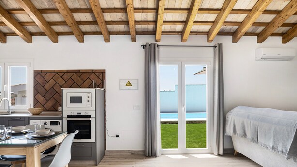 Uma cozinha moderna com micro-ondas, forno e pia, uma área de refeições com mesa e cadeiras, e uma varanda com vista para o mar.